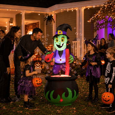 Family and kids trick-or-treating beside the lit up witch cauldron bubbling potion Halloween inflatable at night