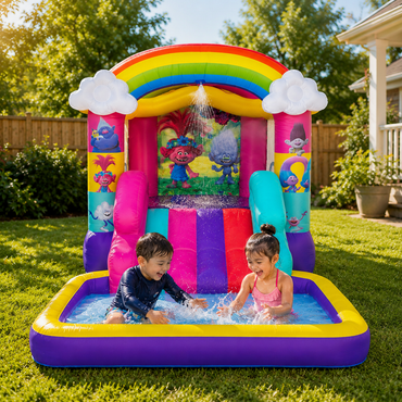 A children's inflatable bounce house pool set in a backyard, with two kids playing in the pool at the base. The inflatable features a rainbow arch, white clouds, colorful side panels with Trollface-themed graphics, a pink and blue slide, and a purple base.