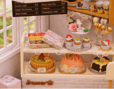 Miniature cake shop display with various cakes and a 'Cake Shop' sign.