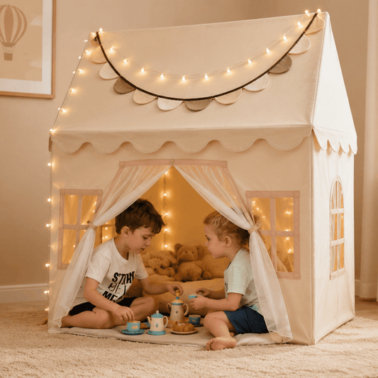 Two children playing inside a white playhouse with string lights in a cozy room.