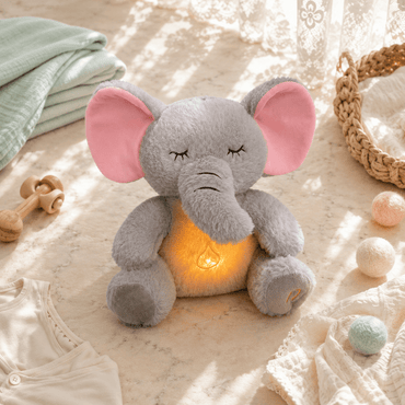 Plush elephant toy with a glowing light inside, surrounded by soft toys and baby items on a textured surface.