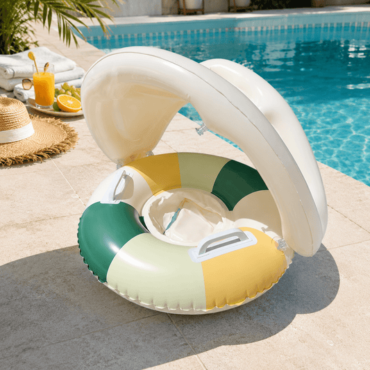 An inflatable baby pool float with a built-in sun canopy sits on a tiled pool deck next to a swimming pool. The float features alternating green, pale yellow, and cream-colored panels, with a white canopy that is open to provide shade.