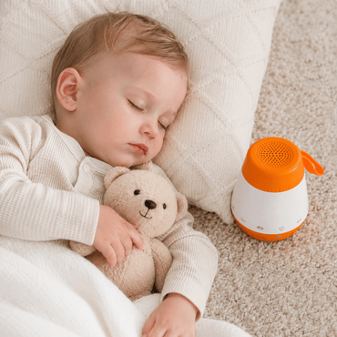 Baby sleeping peacefully with white noise sound machine on nursery floor