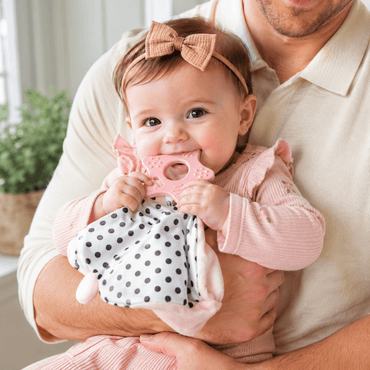 Baby chewing on the teether of a pink bunny lovey comforting blanket while held by dad