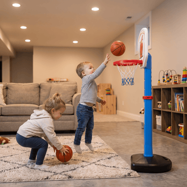 Two toddlers playing with the blue adjustable basketball hoop set in a finished home basement