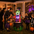 Family and kids trick-or-treating beside the lit up witch cauldron bubbling potion Halloween inflatable at night