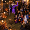 Family and kids in costumes posing for a photo in front of an 8 ft animated flying witch Halloween decoration in a glowing yard