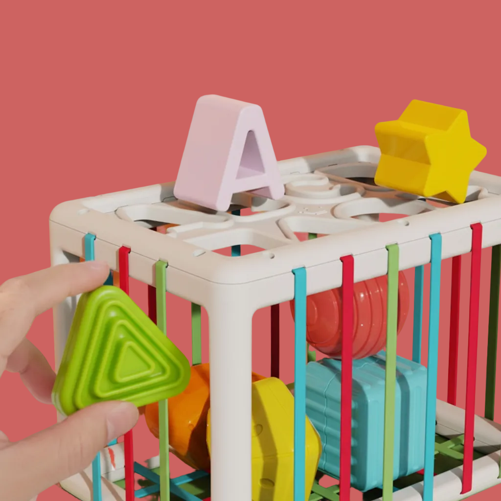 Colorful wooden shape sorter toy with a hand placing a green triangle shape into it against a pink background-Baby_Activity_Cube_-_Montessori_Learning_Toy