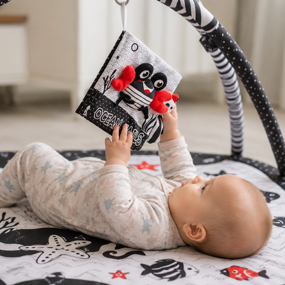 Baby playing with a soft book on a play mat with toys.