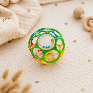Colorful baby toy rattle on a soft surface with wooden toys in the background