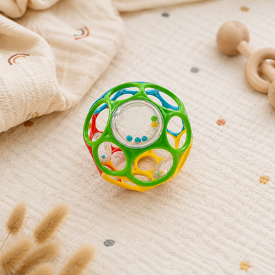 Colorful baby toy rattle on a soft surface with wooden toys in the background