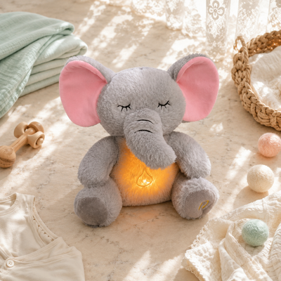 Plush elephant toy with a glowing light inside, surrounded by soft toys and baby items on a textured surface.