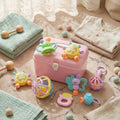 Pink toy suitcase with colorful baby toys on a soft surface