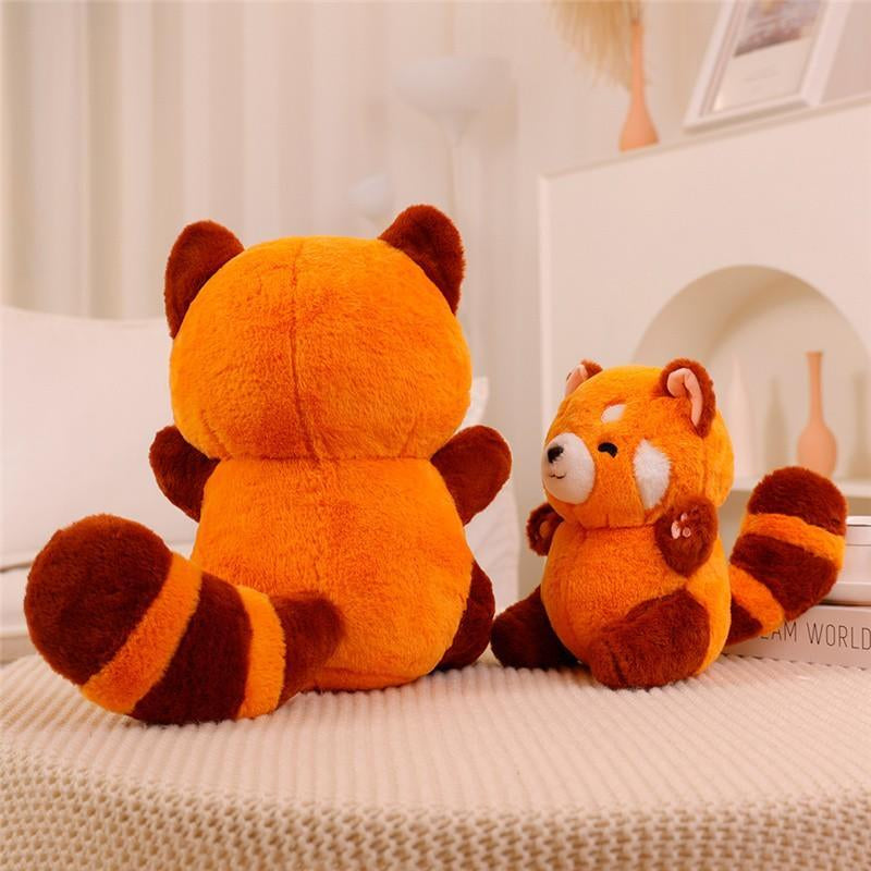 Two plush red pandas sitting on a textured surface with a blurred indoor background.