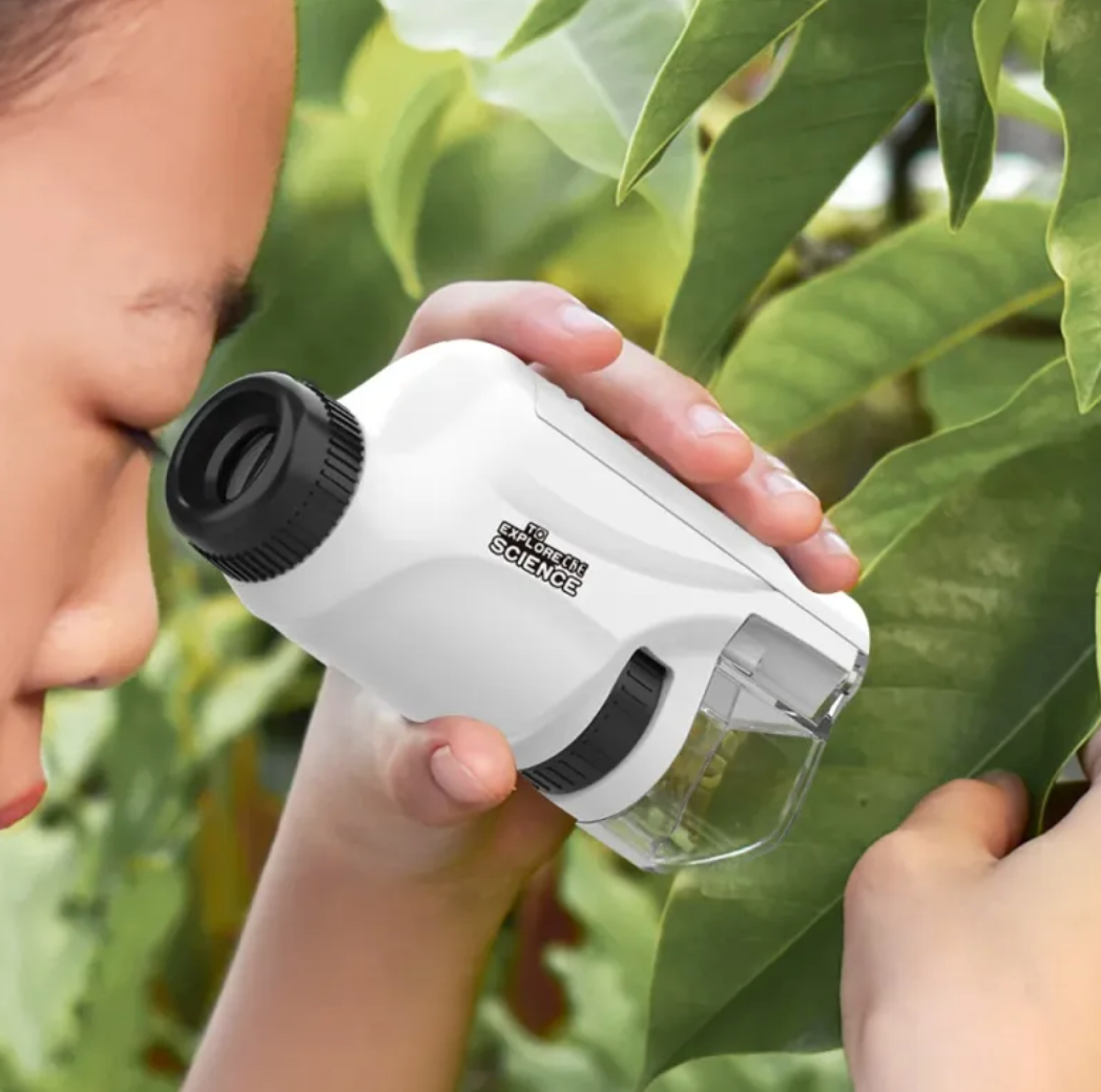 kid using a small white microscope to examine green leaves