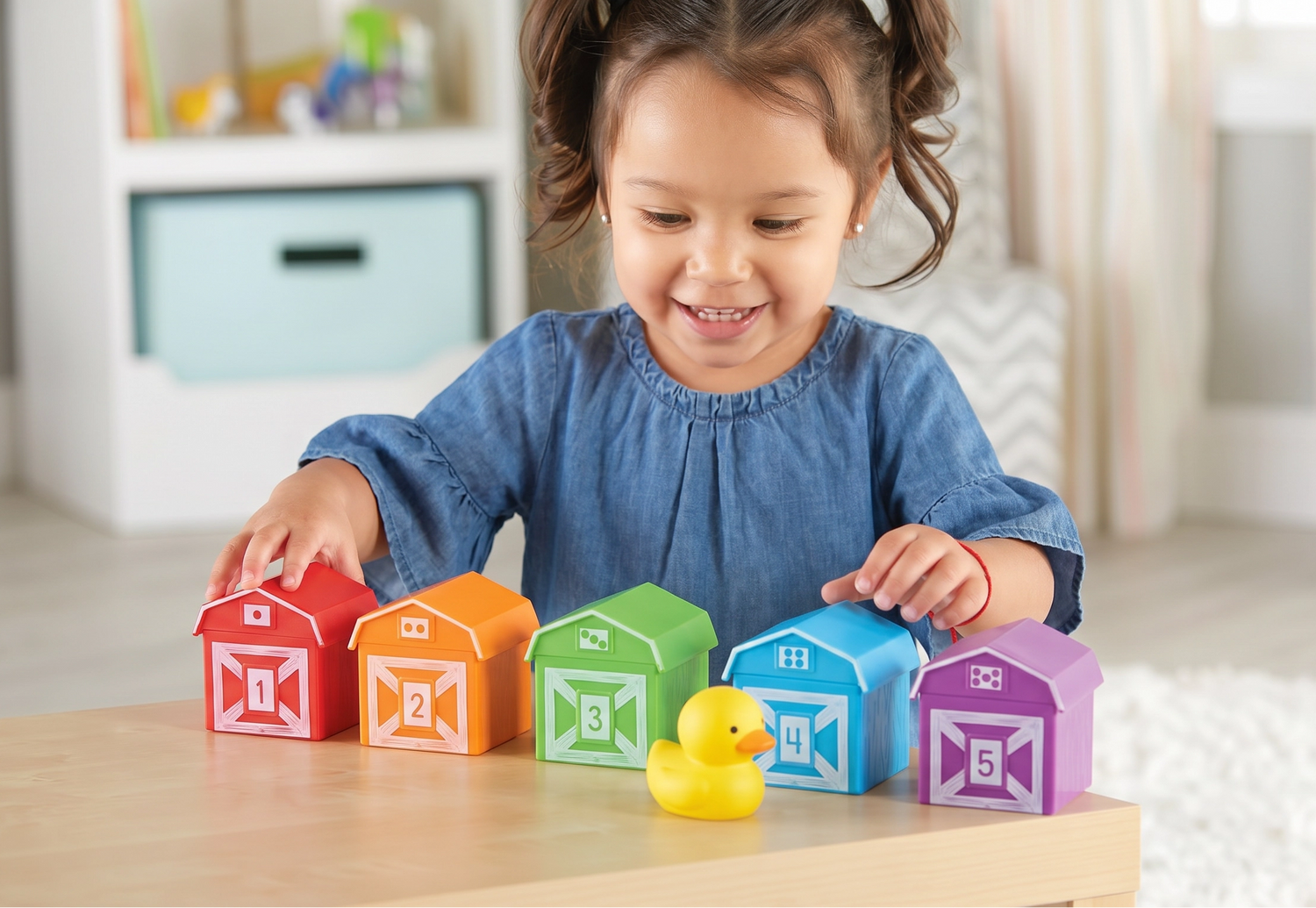 Child playing with colorful toy houses and a rubber duck on a wooden table.