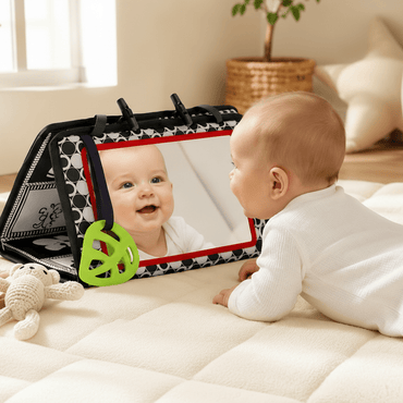 Baby playing with a mirror and toy on a mat in a room.