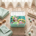 Set of baby toys in a blue container on a marble surface with clothes and balls around