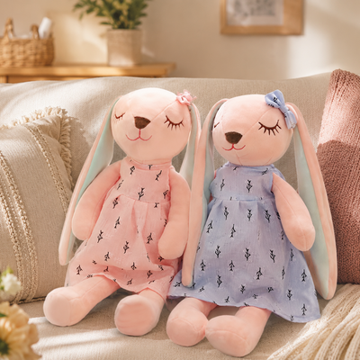 Two plush toys with bunny ears and dresses sitting on a couch.