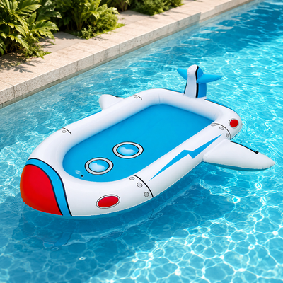 A cartoon-style inflatable pool float shaped like a spaceship, floating on clear blue swimming pool water next to a tiled edge with green plants.