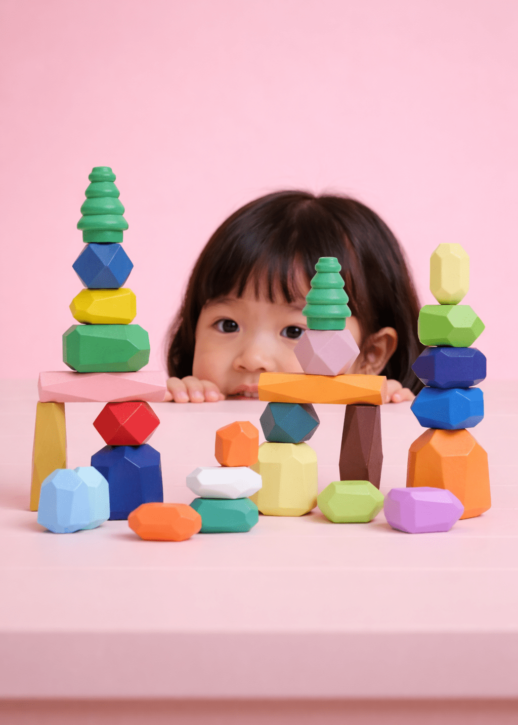 Girl peeking over stacked towers of wooden balancing stones.