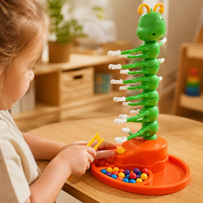 A child's hands and head are visible as they play with a green caterpillar-shaped toy on an orange base, with colorful beads in a tray, set on a wooden table in a softly blurred indoor room.