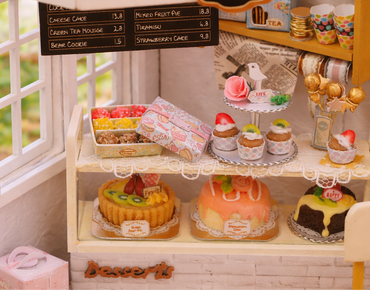Miniature cake shop display with various cakes and a 'Cake Shop' sign.
