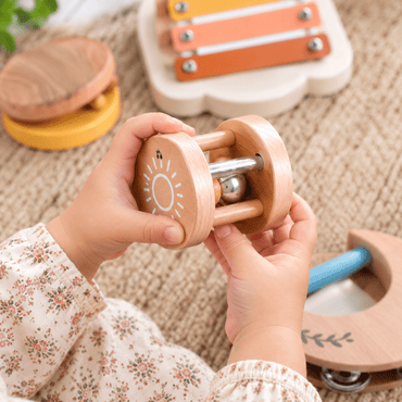 Toddler hands holding a wooden sun rattle bell from the musical instrument set