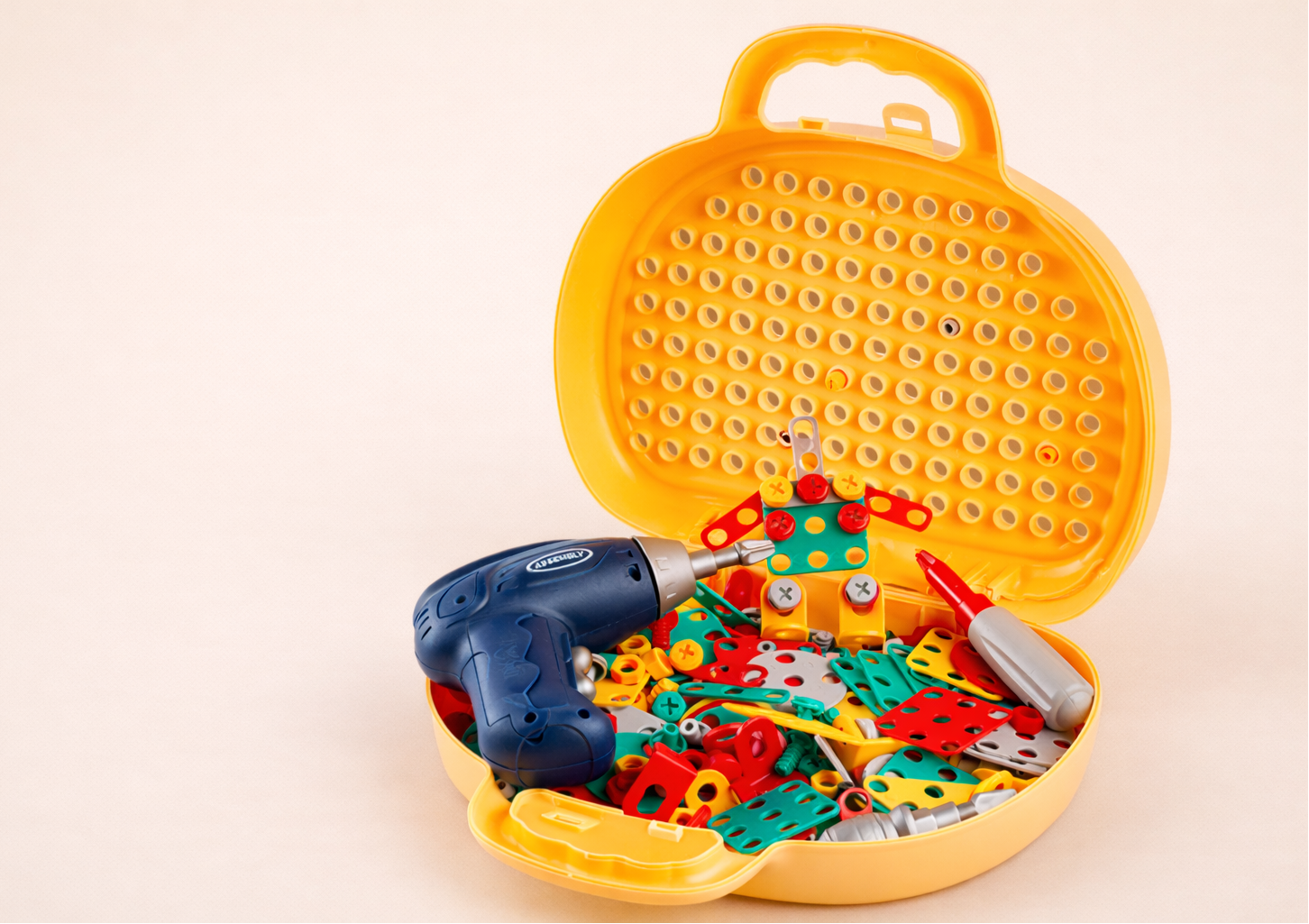 Toy tool set with colorful tools and a drill in a yellow toolbox on a beige background